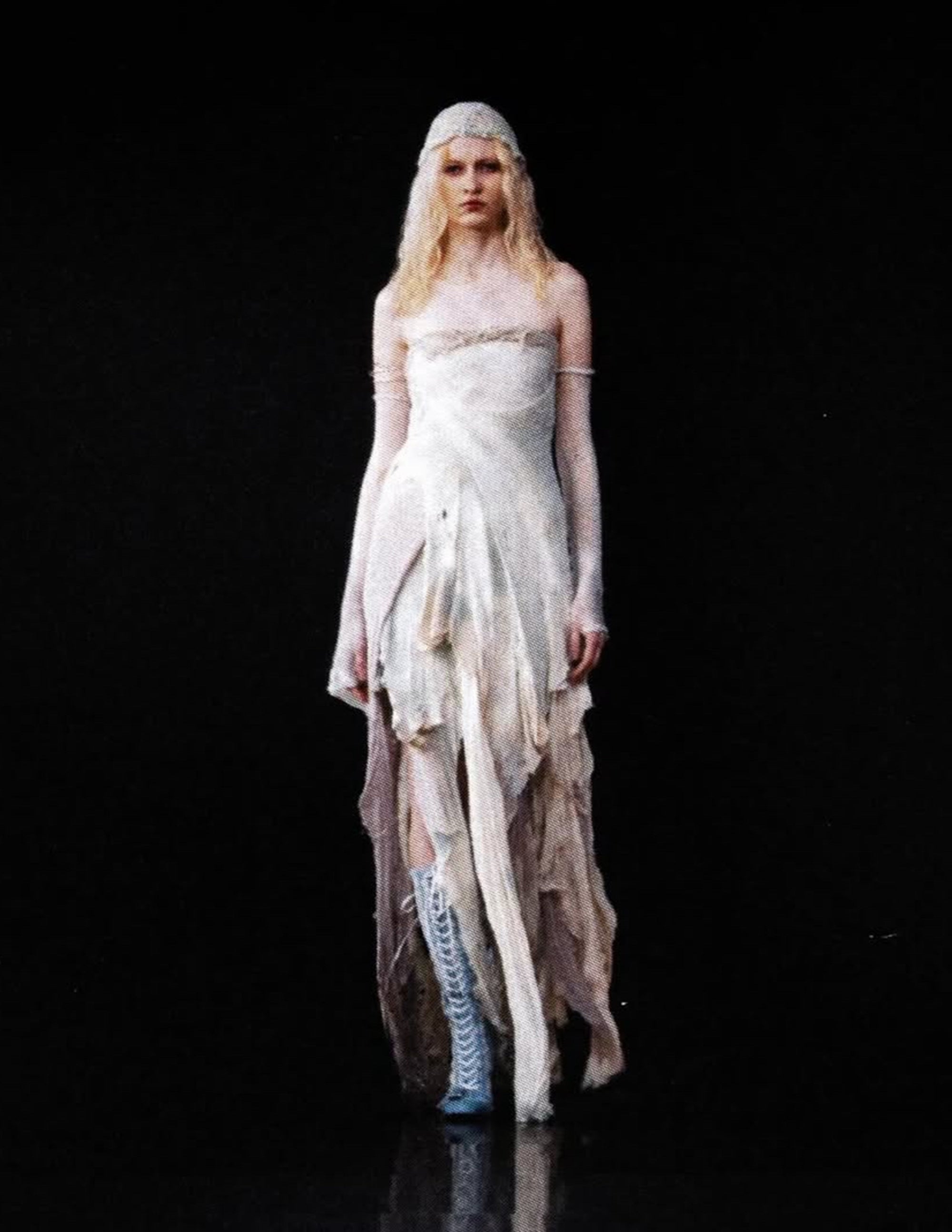 Model wearing a white, flowing dress with long sleeves and a headpiece on a black background