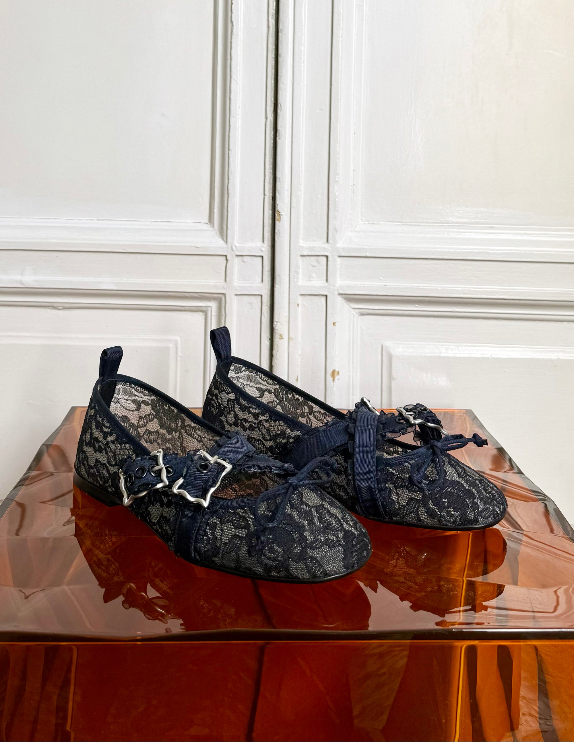 Pair of navy lace shoes on a reflective surface with a white paneled wall background