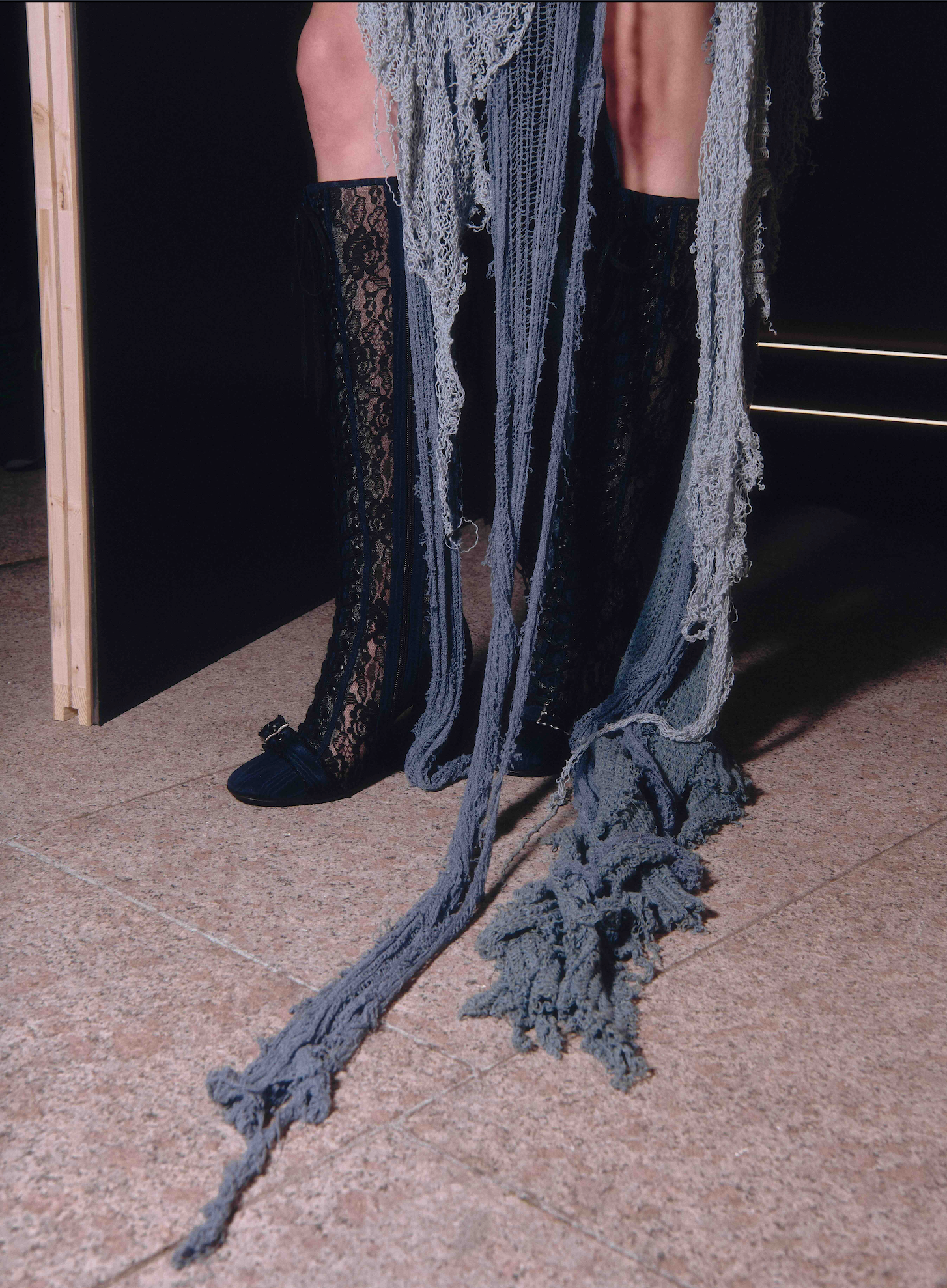 Black knee-high boots with lace detailing on a textured floor.